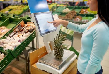 shopping, sale, consumerism and people concept - woman weighing pineapple on scale at grocery store